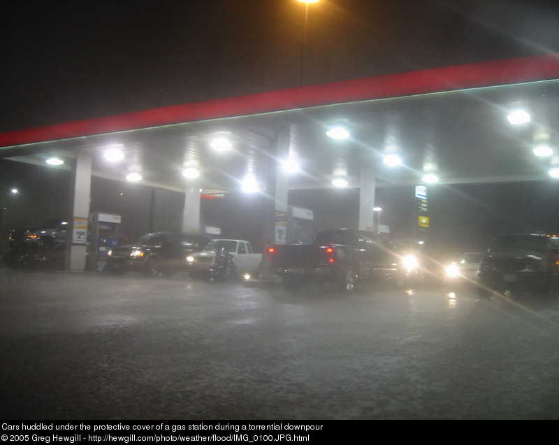 Cars huddled under the protective cover of a gas station during a torrential downpour